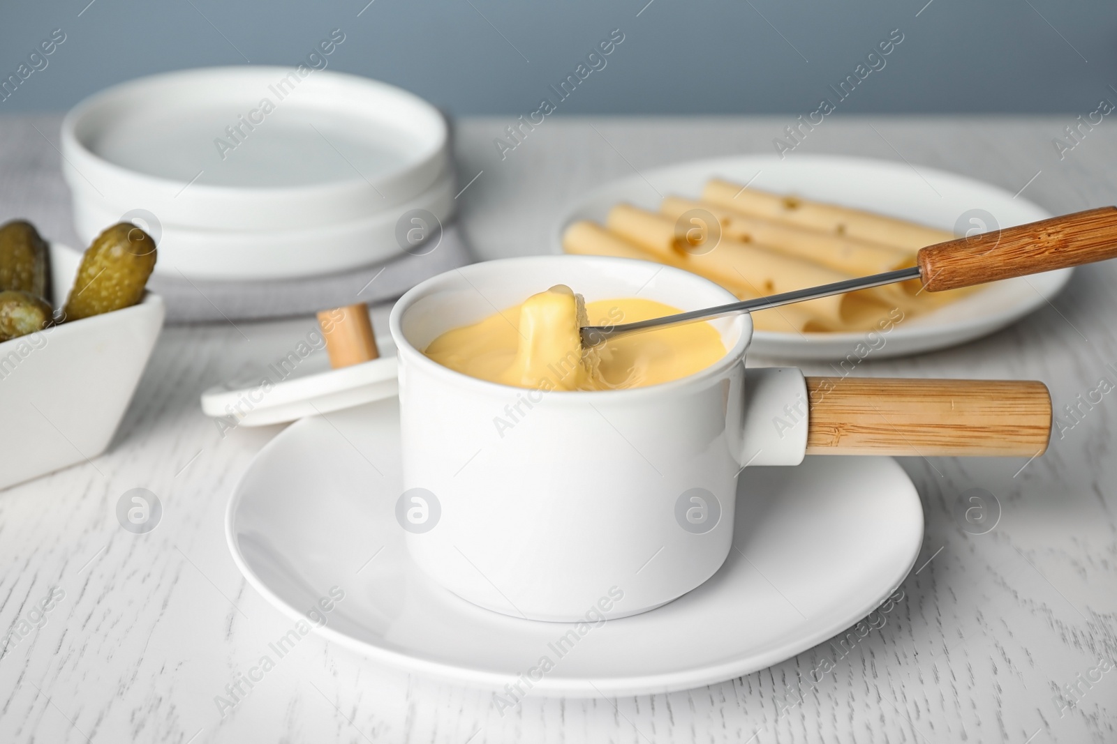 Photo of Pot of tasty cheese fondue and fork with bread on white wooden table