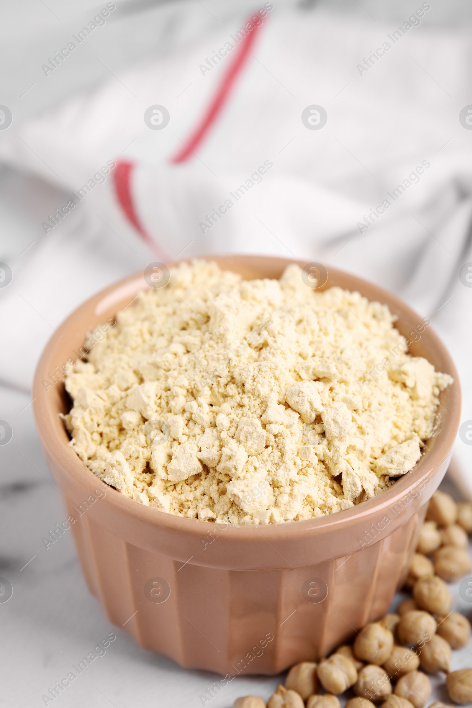 Photo of Chickpea flour in bowl and seeds on white marble table, closeup