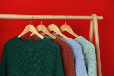 Collection of warm sweaters hanging on rack near red wall