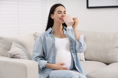 Pregnant woman drinking from cup on sofa at home