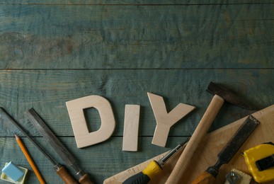 Photo of Abbreviation DIY made of letters and different tools on grey wooden table, flat lay. Space for text