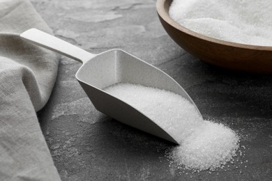 Photo of Granulated sugar in scoop on grey textured table, closeup