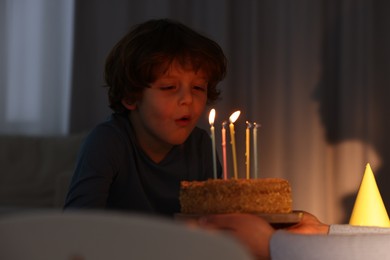 Photo of Birthday celebration. Mother holding tasty cake with burning candles near her son indoors