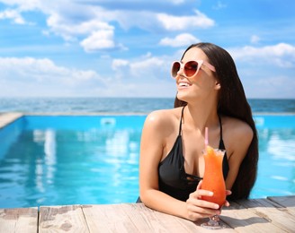 Image of Beautiful young woman with cocktail in outdoor swimming pool at luxury resort  