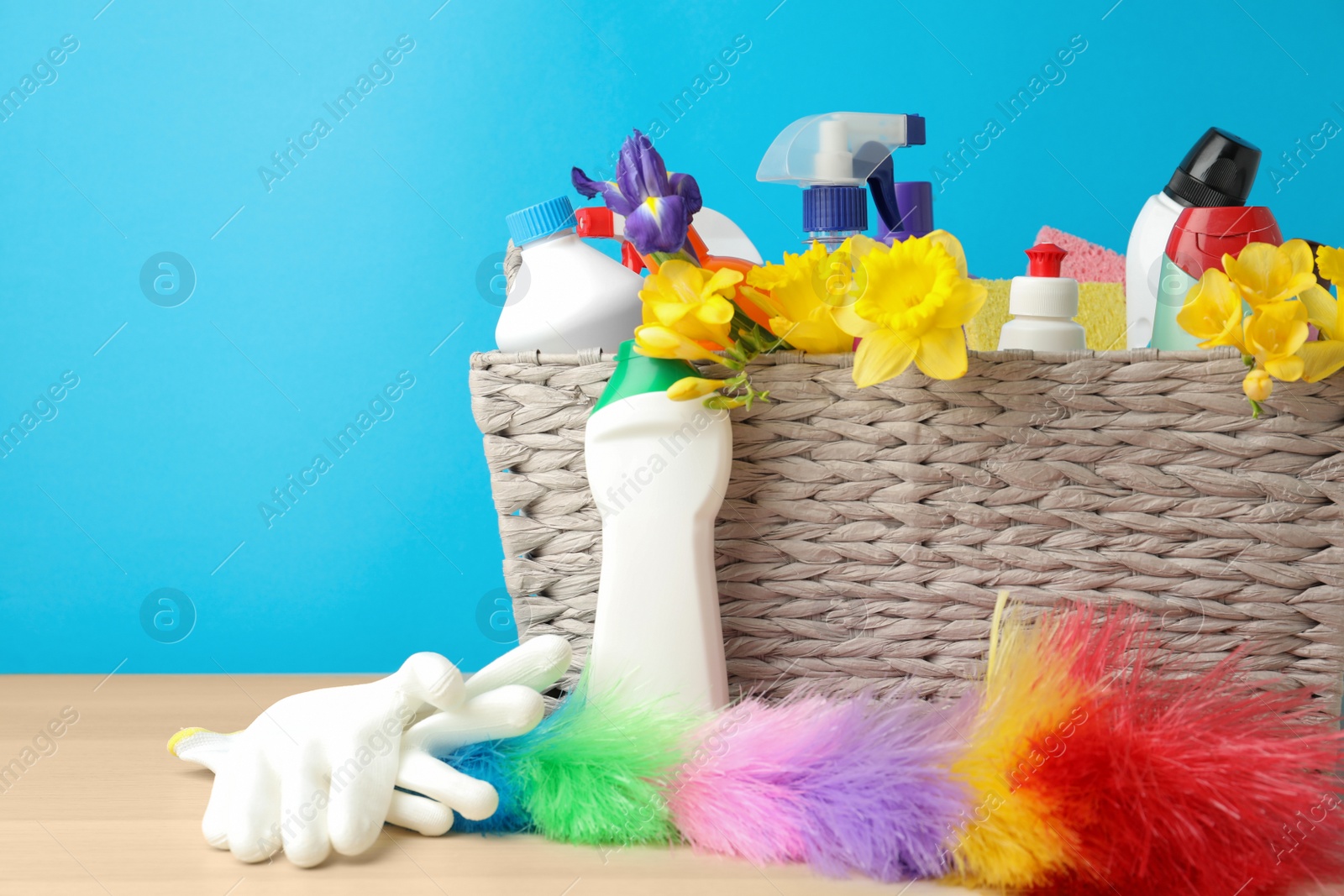 Photo of Wicker basket with spring flowers and cleaning supplies on wooden table