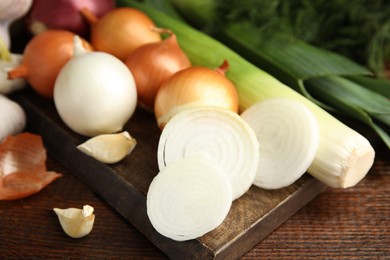 Fresh onion bulbs, leeks, garlic on wooden table, closeup