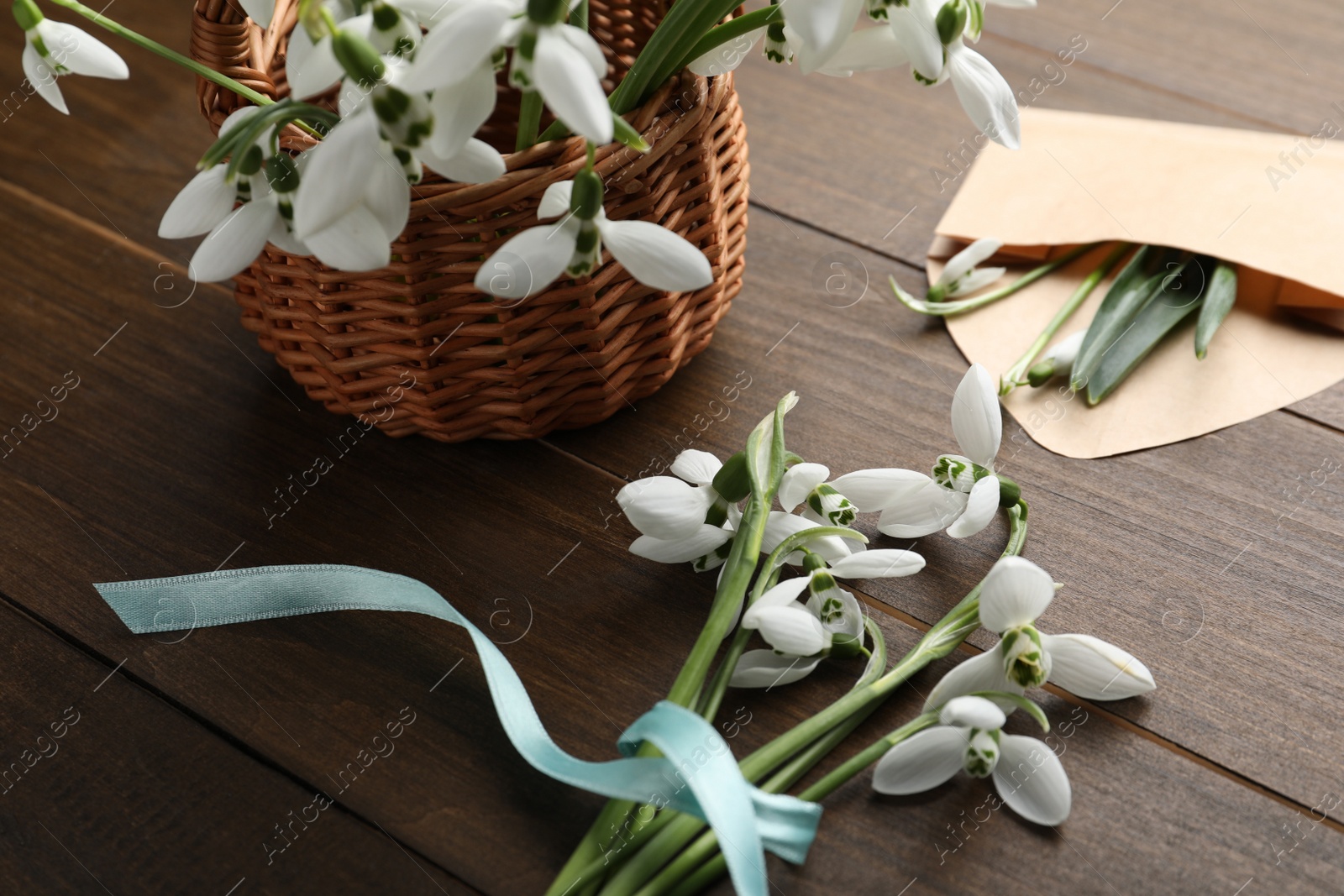 Photo of Beautiful snowdrops with wicker basket and envelope on wooden table