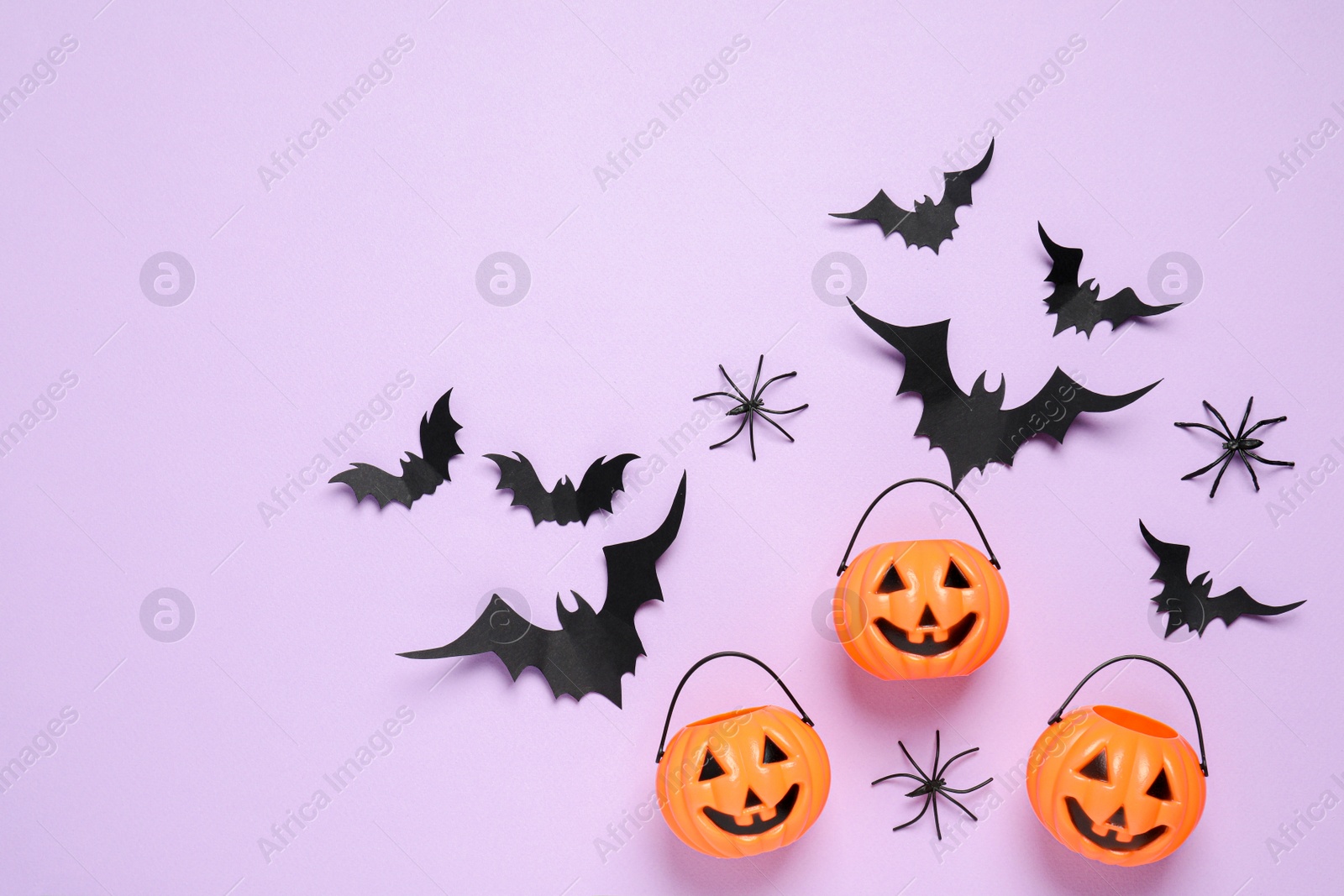 Photo of Flat lay composition with paper bats, plastic pumpkin baskets and spiders on light violet background, space for text. Halloween decor