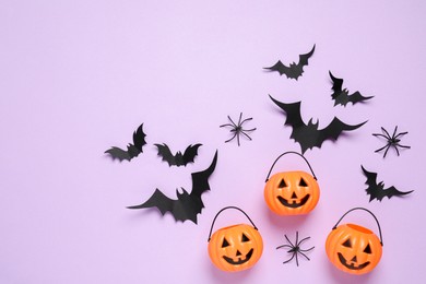 Photo of Flat lay composition with paper bats, plastic pumpkin baskets and spiders on light violet background, space for text. Halloween decor