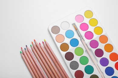 Photo of Watercolor palette and colorful pencils on white background, flat lay