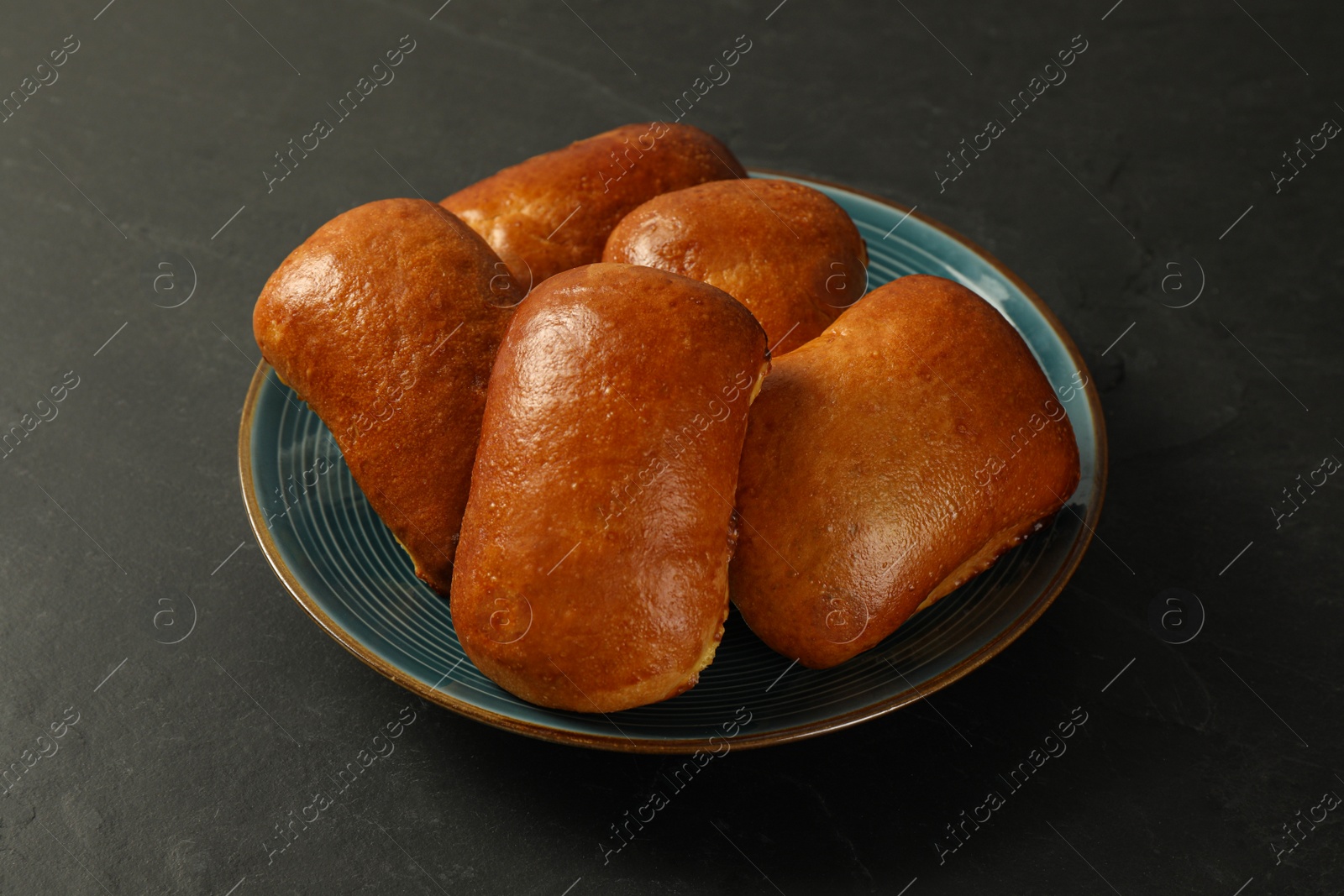 Photo of Many delicious baked pirozhki on black table