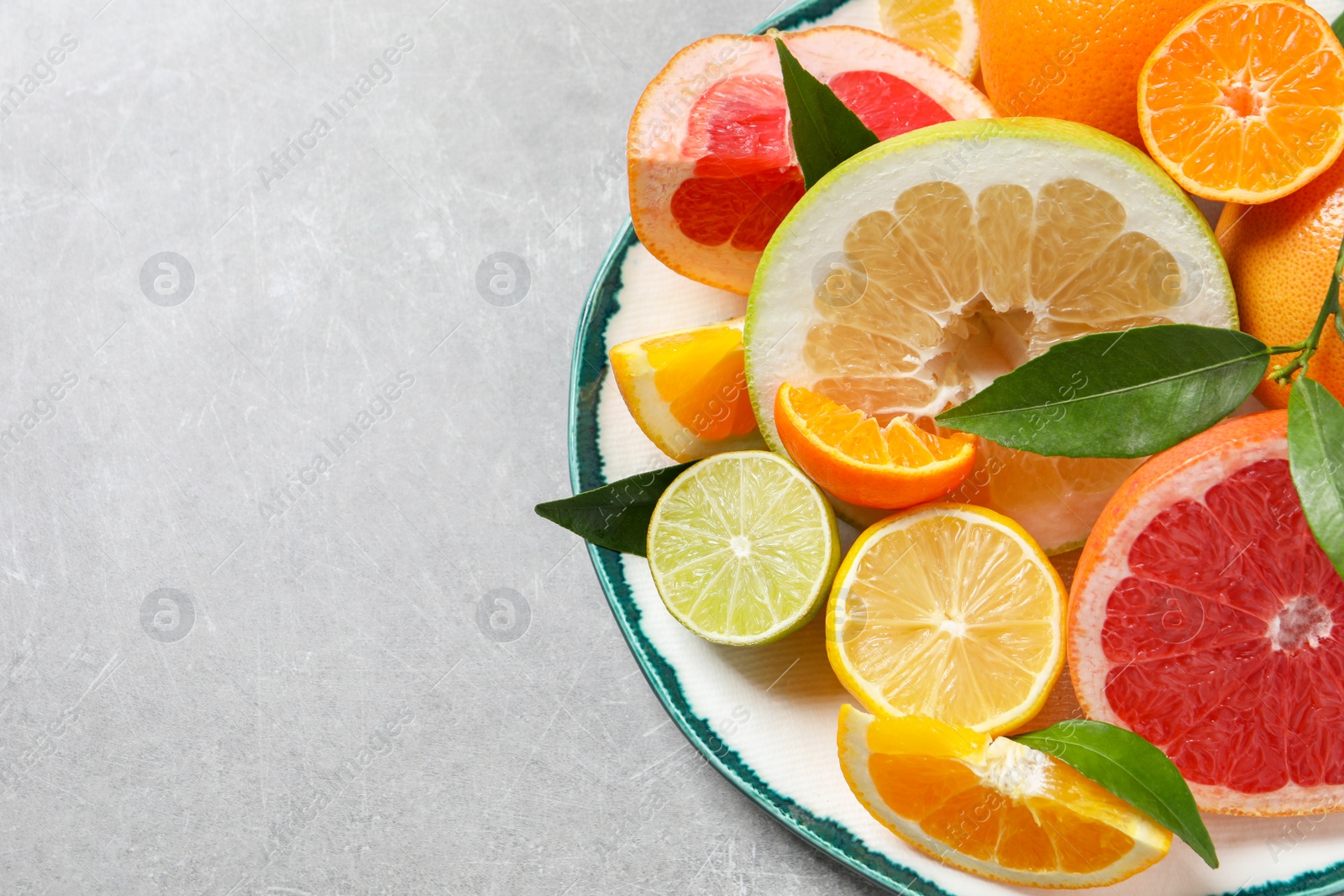 Photo of Plate with different citrus fruits and fresh leaves on light grey table, top view. Space for text