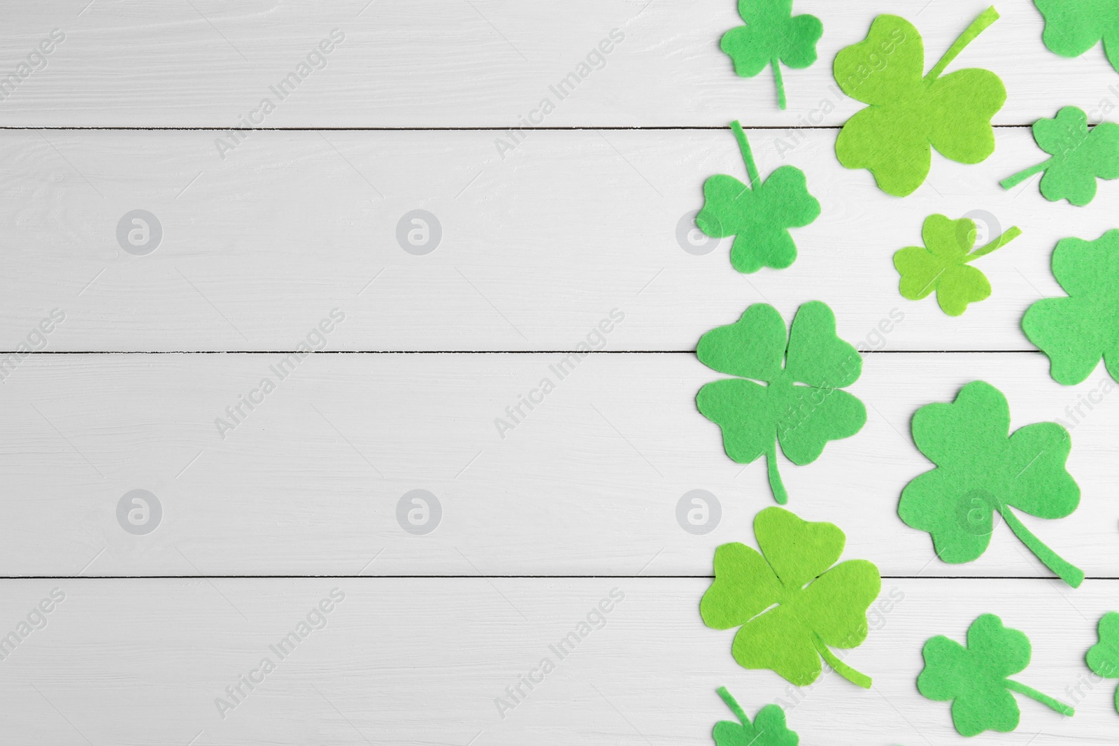 Photo of St. Patrick's day. Decorative green clover leaves on white wooden table, flat lay. Space for text