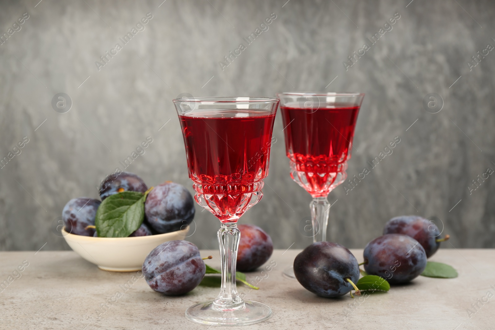 Photo of Delicious plum liquor and ripe fruits on table against grey background. Homemade strong alcoholic beverage