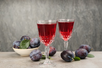 Photo of Delicious plum liquor and ripe fruits on table against grey background. Homemade strong alcoholic beverage