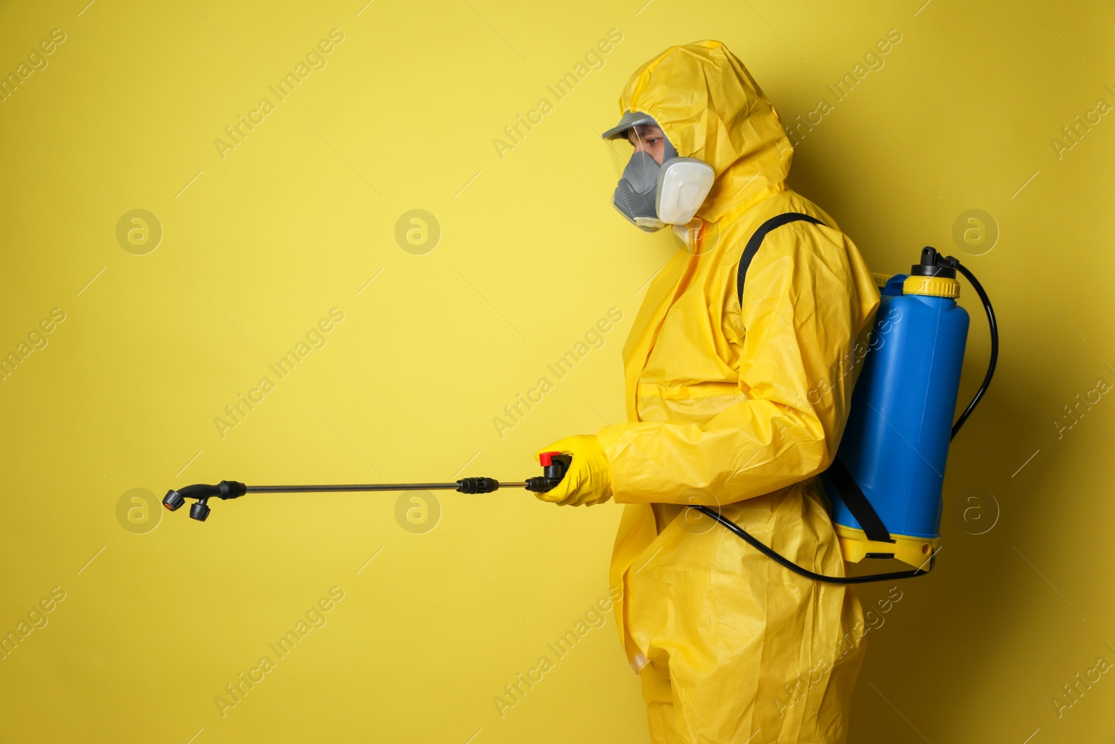 Photo of Man wearing protective suit with insecticide sprayer on yellow background. Pest control