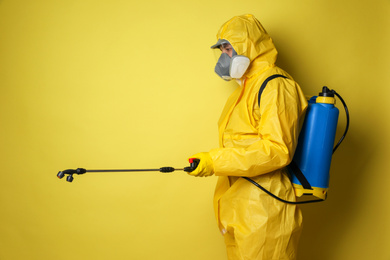 Photo of Man wearing protective suit with insecticide sprayer on yellow background. Pest control