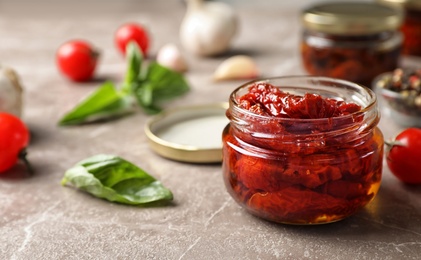 Photo of Dried tomatoes in glass jar on table. Healthy snack