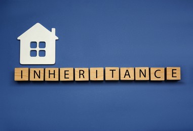 Photo of Word Inheritance made with wooden cubes and house model on blue background, flat lay