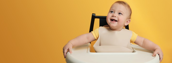 Image of Cute little baby wearing bib in highchair on yellow background, space for text. Banner design