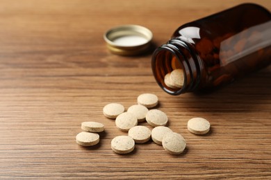 Photo of Overturned bottle with dietary supplement pills on wooden table. Space for text