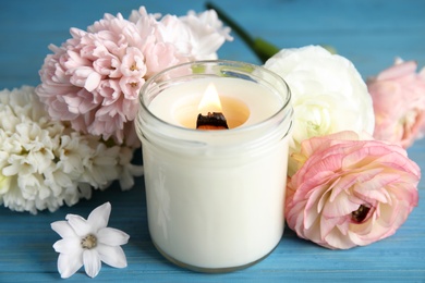 Photo of Scented candle with burning wooden wick and flowers on blue table, closeup