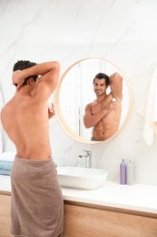 Photo of Handsome young man applying deodorant in bathroom