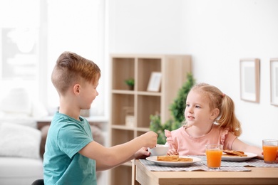 Adorable little children eating tasty toasted bread with jam at table