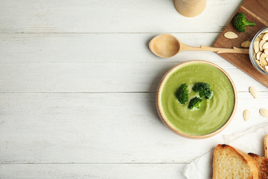 Photo of Delicious broccoli cream soup served on white wooden table, flat lay. Space for text