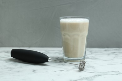 Photo of Mini mixer (milk frother) and tasty cappuccino in glass on white marble table