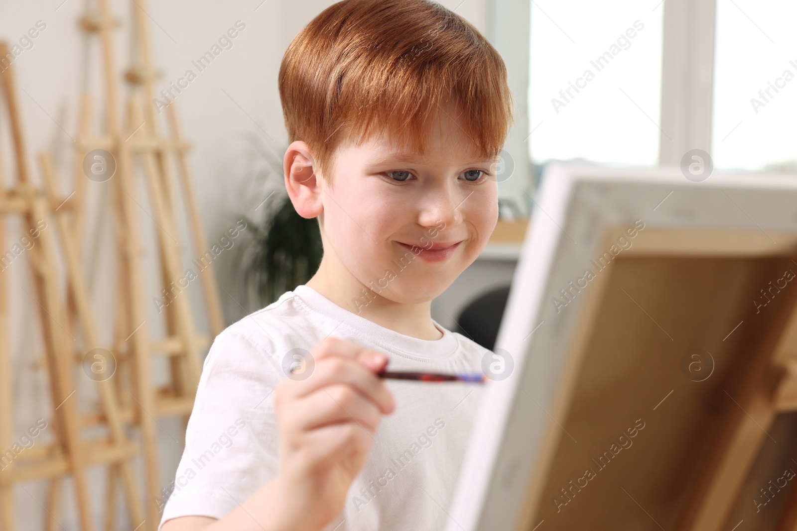 Photo of Little boy painting on canvas in studio