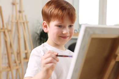 Photo of Little boy painting on canvas in studio