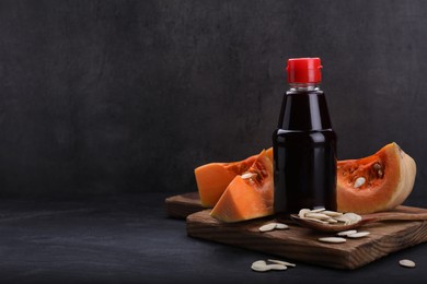 Photo of Fresh pumpkin seed oil in glass bottle on dark grey table. Space for text