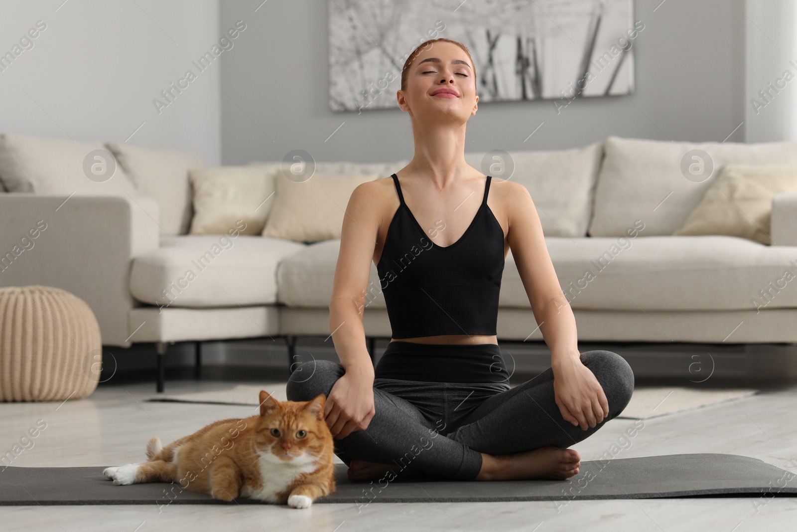 Photo of Beautiful woman with cute red cat practicing yoga on mat at home