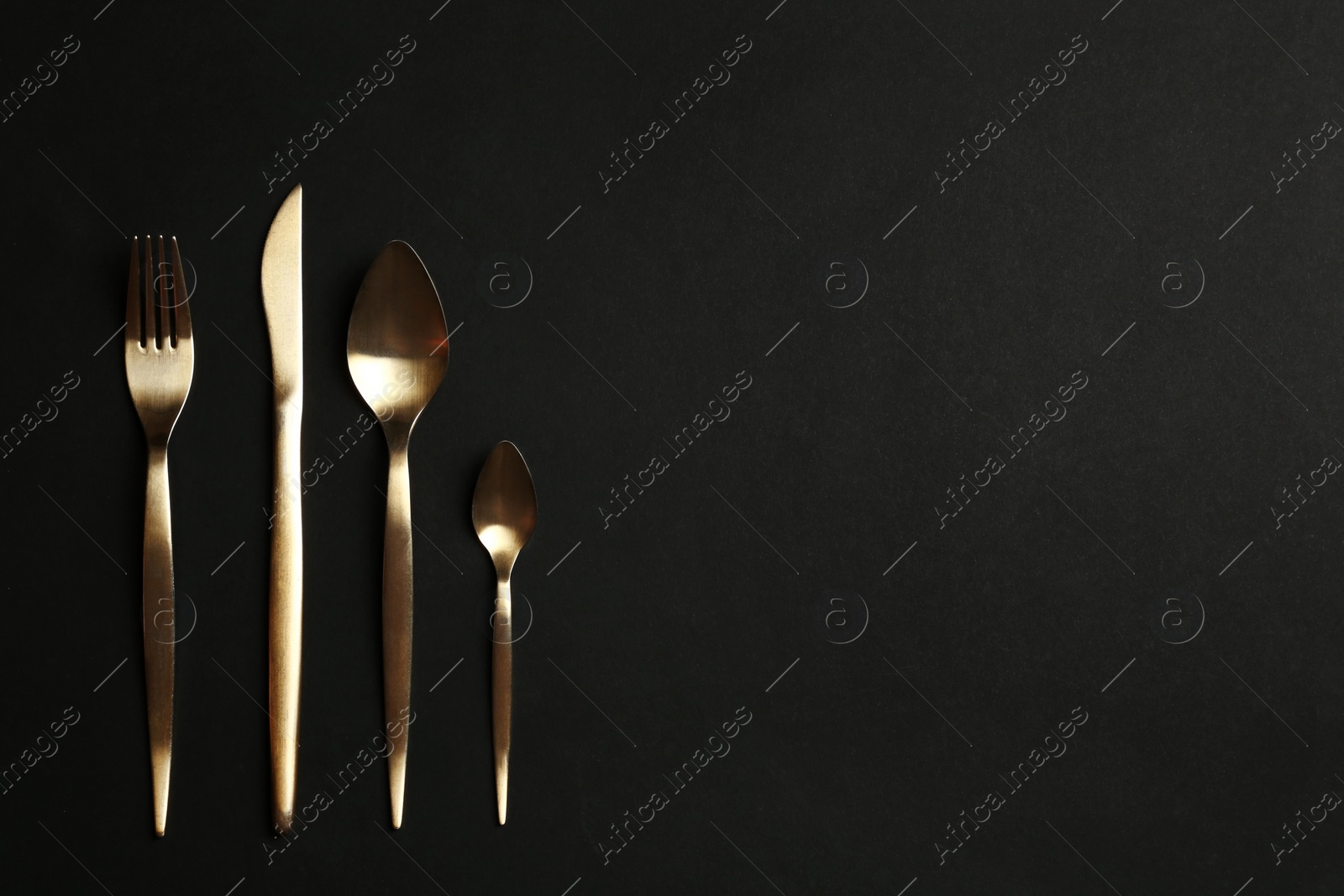 Photo of Set of gold cutlery on black background, flat lay. Space for text