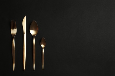 Photo of Set of gold cutlery on black background, flat lay. Space for text