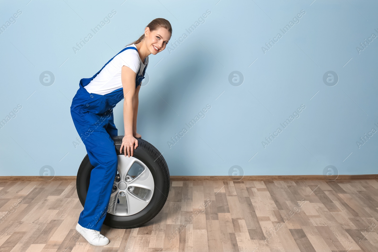 Photo of Female mechanic with car tire on grey wall background