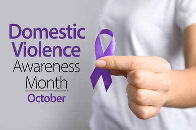 Woman holding purple ribbon on grey background, closeup. Symbol of Domestic Violence Awareness