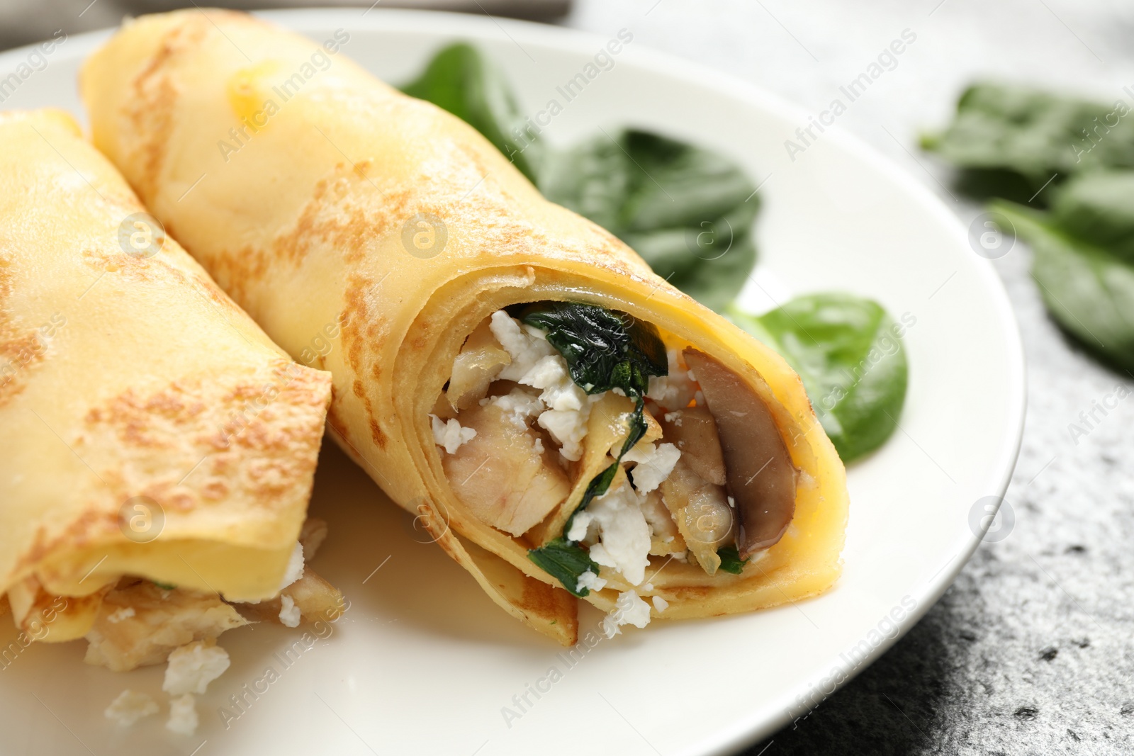 Photo of Delicious thin pancakes with chicken and mushrooms on grey table, closeup