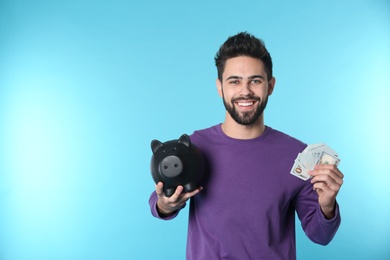 Photo of Happy young man with money and piggy bank on color background. Space for text