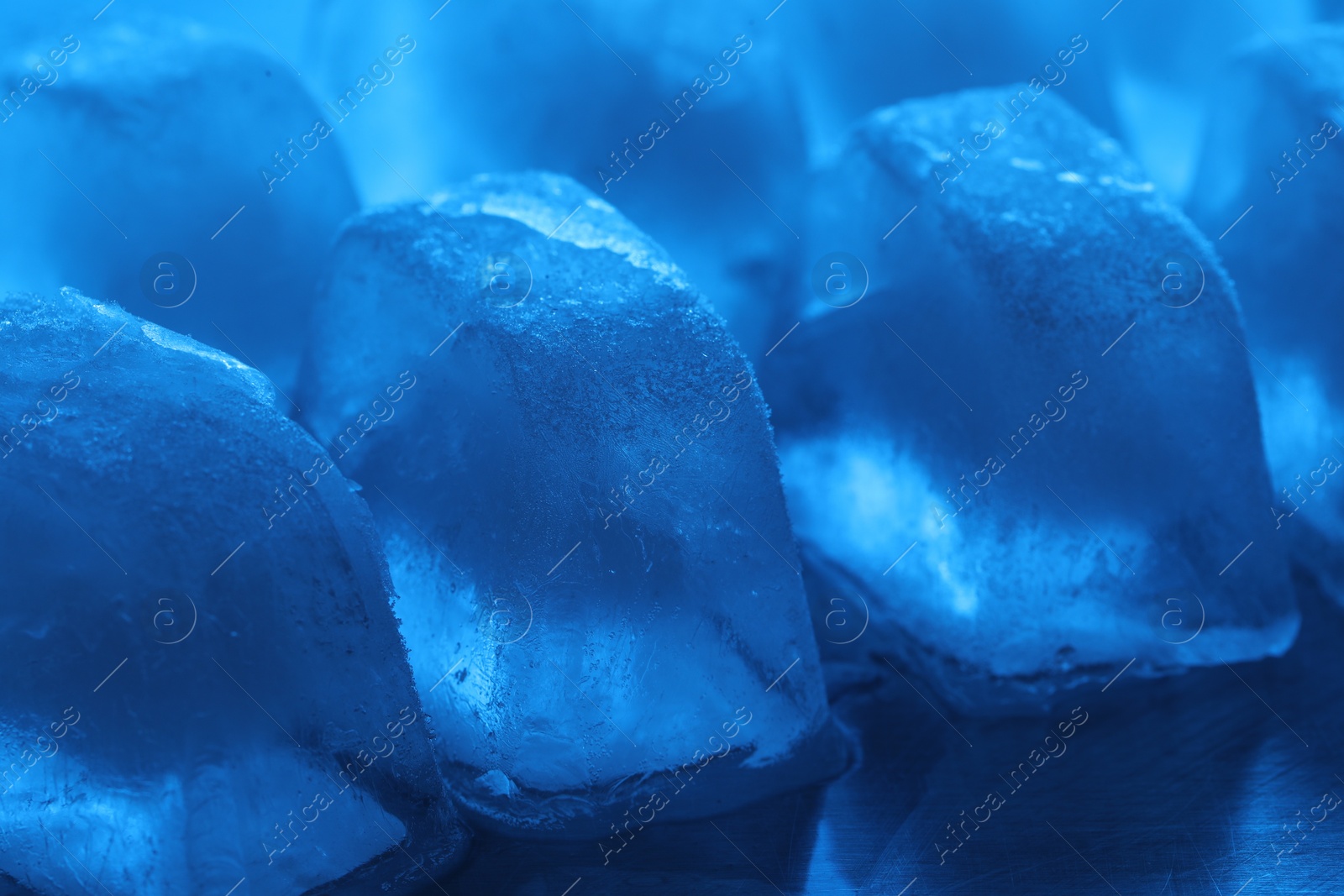 Photo of Crystal clear ice cubes on light blue background, closeup. Color tone effect