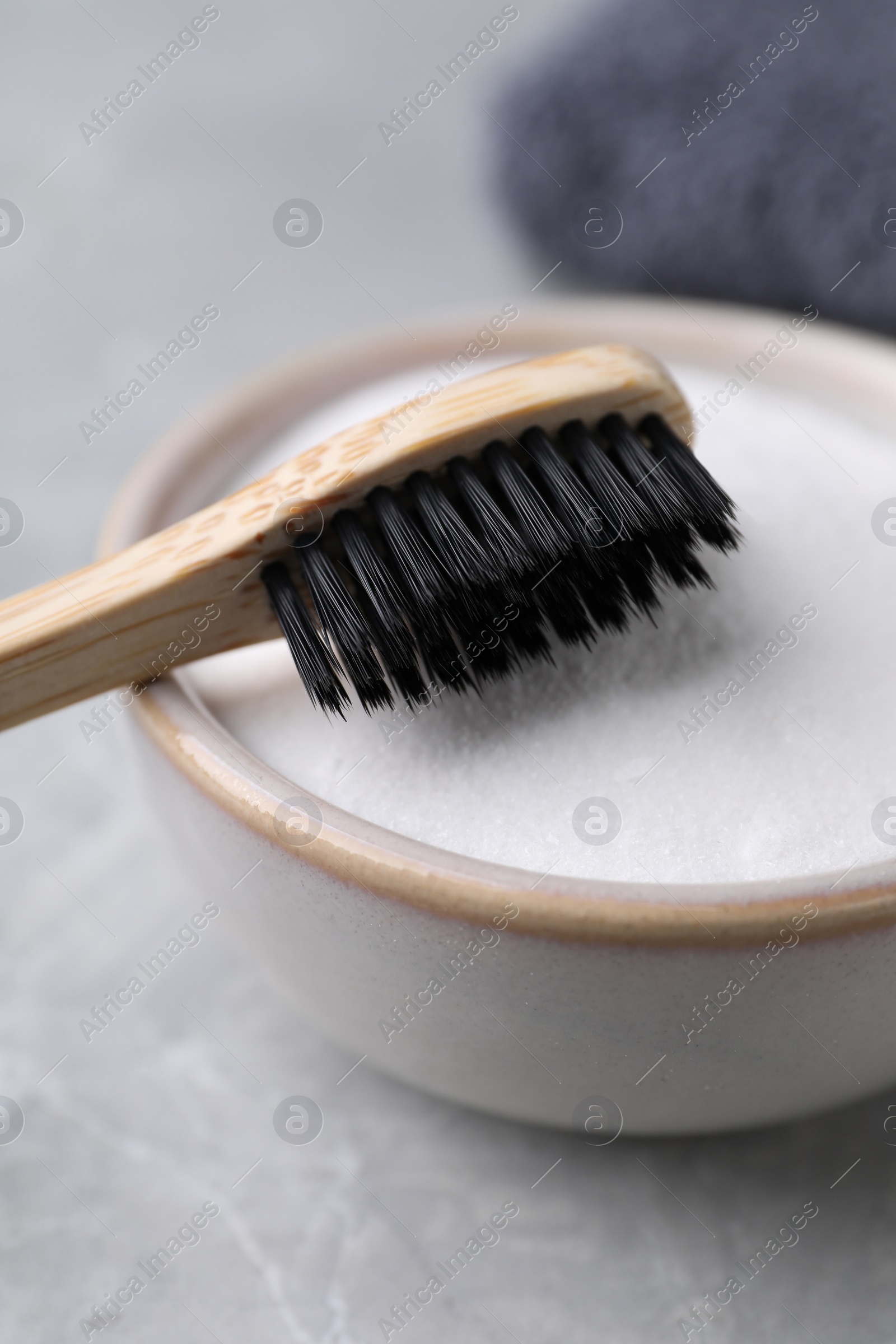 Photo of Bamboo toothbrush and bowl of baking soda on light grey table, closeup
