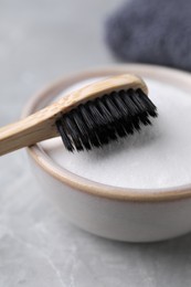 Bamboo toothbrush and bowl of baking soda on light grey table, closeup