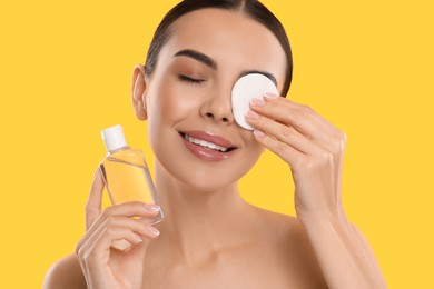 Photo of Beautiful woman removing makeup with cotton pad on yellow background