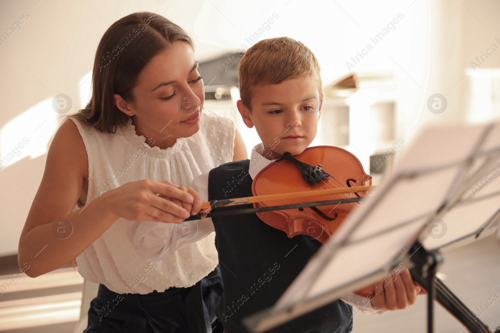 Photo of Young woman teaching little boy to play violin indoors