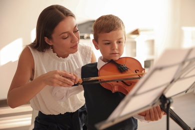 Photo of Young woman teaching little boy to play violin indoors