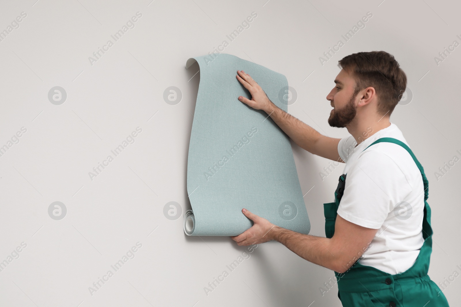 Photo of Worker hanging stylish wall paper sheet indoors. Space for text