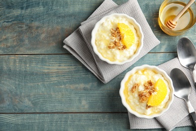Photo of Creamy rice pudding with walnuts and orange in ramekins served on wooden table, top view. Space for text