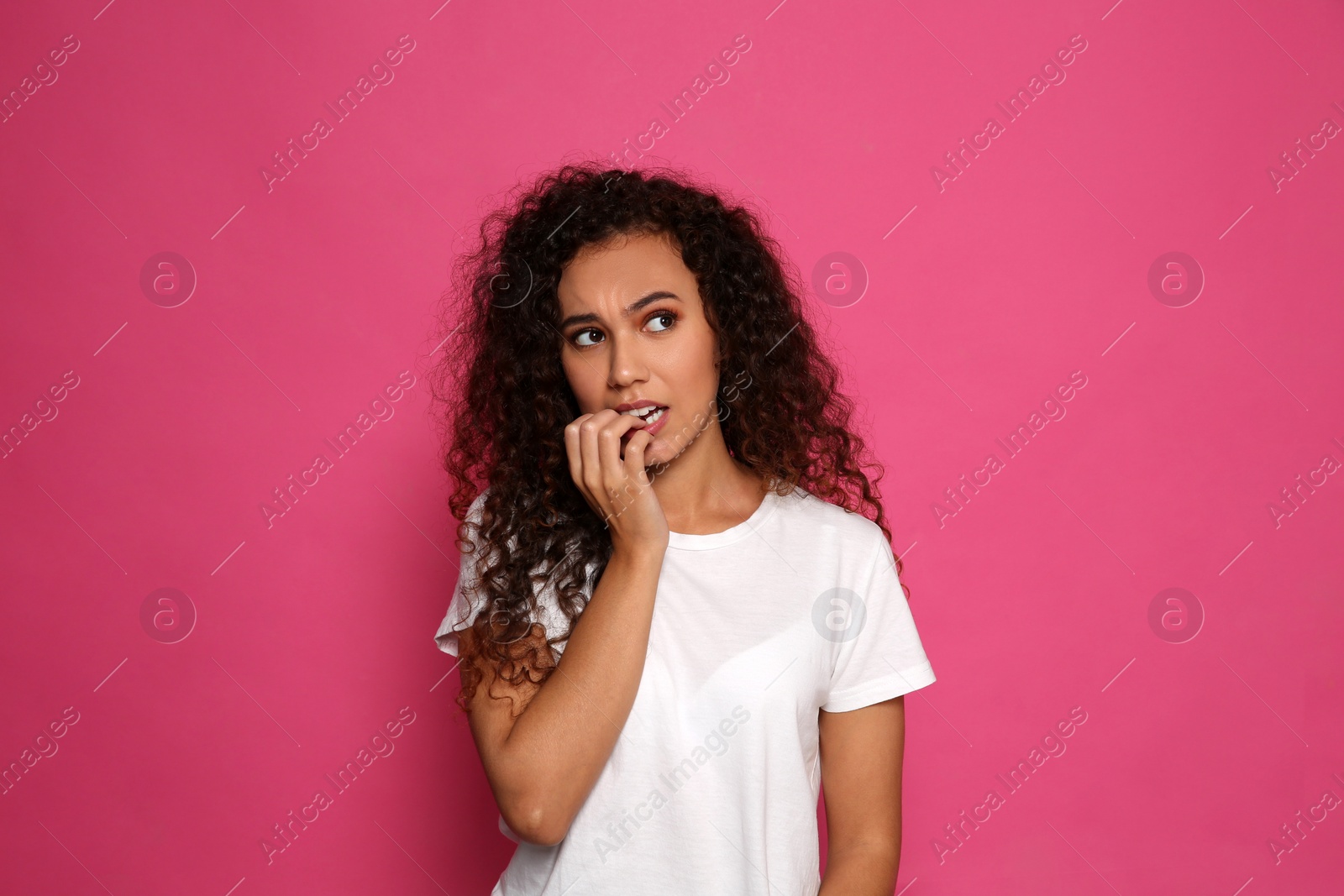 Photo of African-American woman biting her nails on pink background