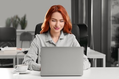 Happy woman working with laptop at white desk in office